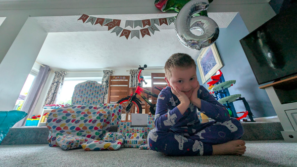 A child sat in front of presents with a balloon in the shape of a number 6 and a bike in the background